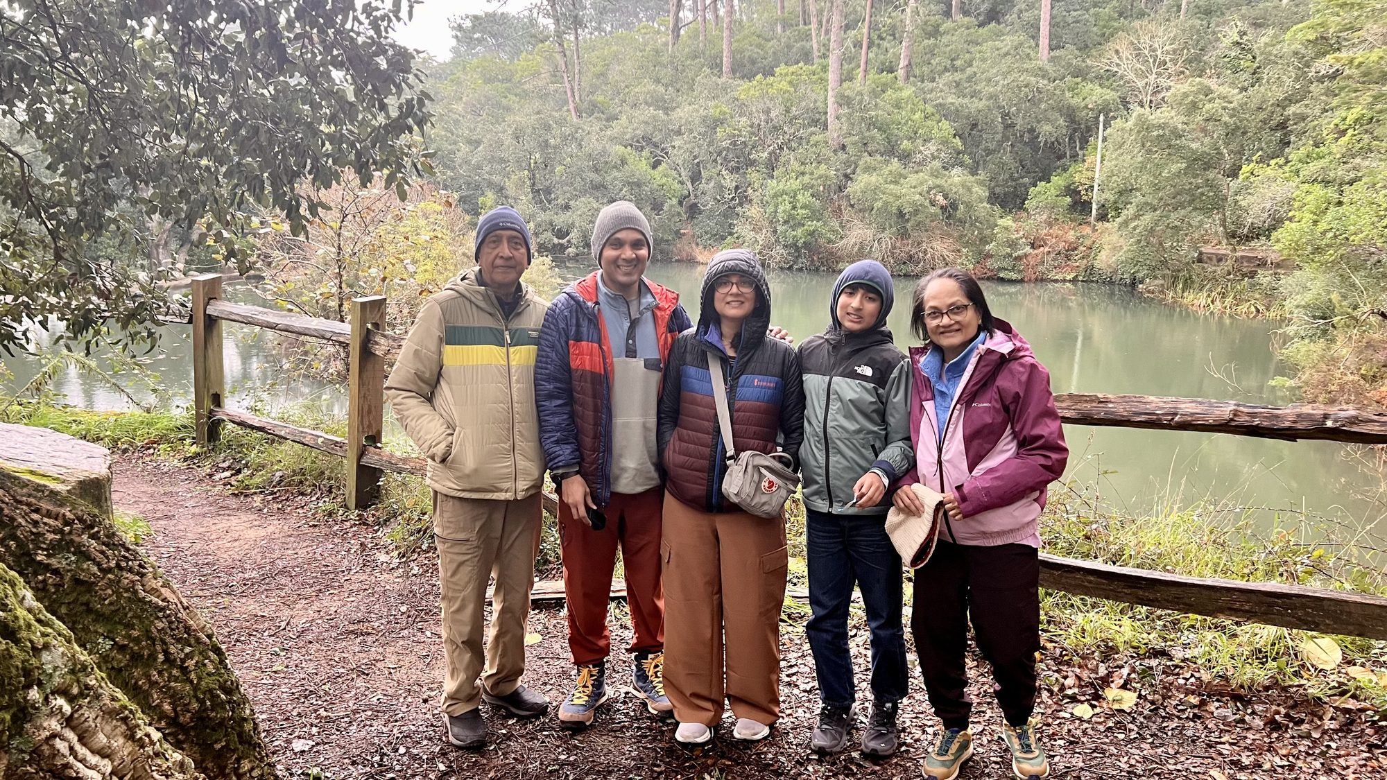 Five of us in hats and jackets on a path beside a lake, with cork trees and forest behind.