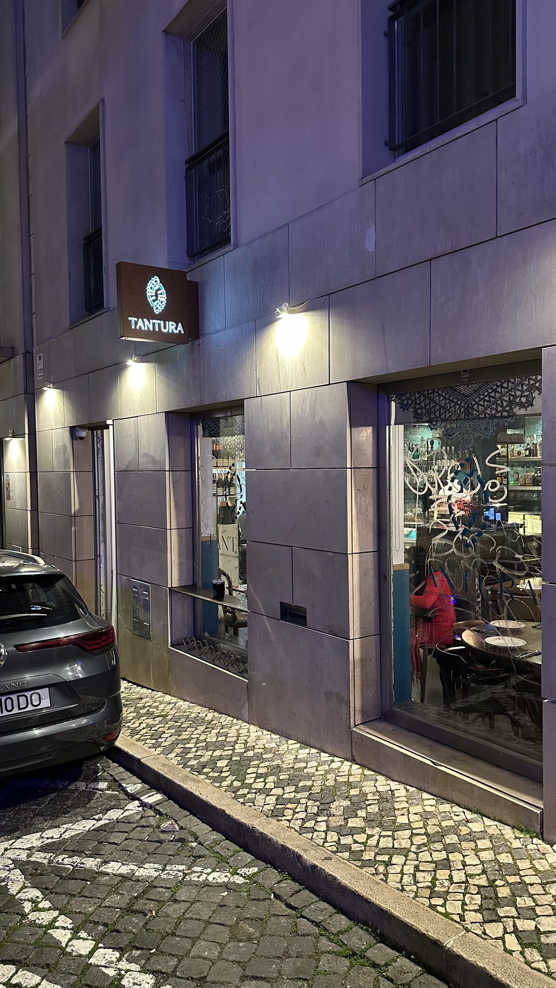 The lit front windows of Tantura restaurant on a quiet cobbled street at dusk.