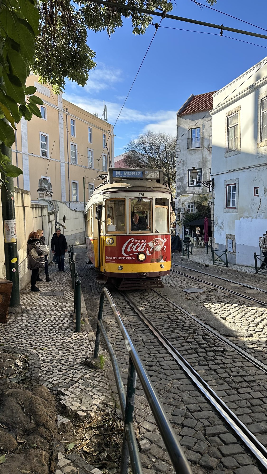 A yellow tram climbing a cobbled street lined with pastel buildings.